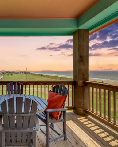 Covered oceanfront deck with Adirondack chairs overlooking beach and sunset sky