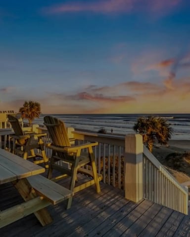 Beachfront deck with yellow Adirondack chairs, white railing, and ocean view at sunset