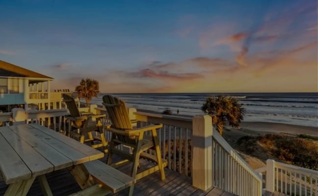 Beachfront deck with yellow Adirondack chairs, white railings, and ocean view at sunset